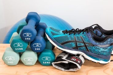 Zdjęcie przedstawiające hantle do ćwiczeń, buty sportowe oraz piłkę