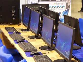Zdjęcie przedstawiające biurka na których stoją monitory z klawiaturami i myszkami
