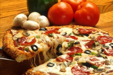 Zdjęcie przekrojonej pizzy z pomidorami, oliwkami i pieczarkami